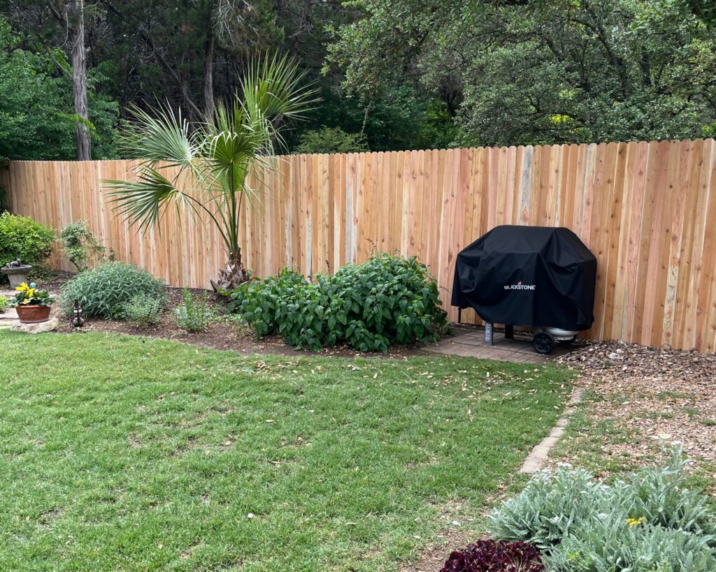 austin-fence-deck-warranty-photo Backyard with a new cedar privacy fence and covered grill beside landscaped greenery in Austin, Texas