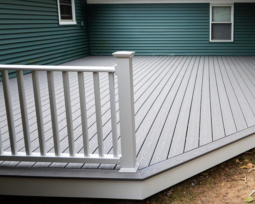 Light gray composite deck with white railing against a green house exterior