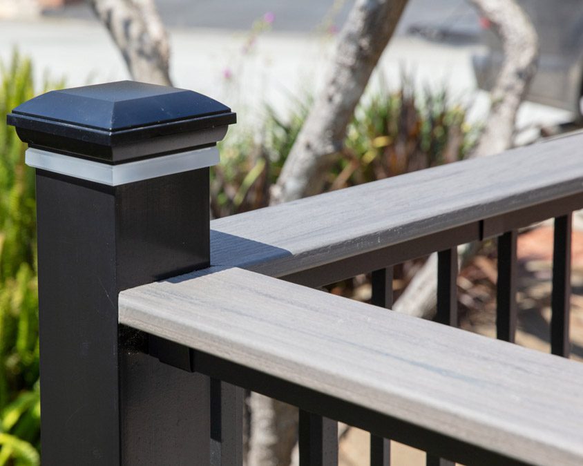 Stock image of a TimberTech® composite drink rail with dark post and flat top rail, overlooking a wooded area.