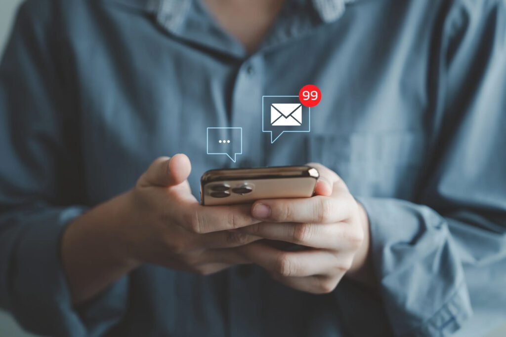 Person in casual workwear holding a phone and reviewing emails or messages.