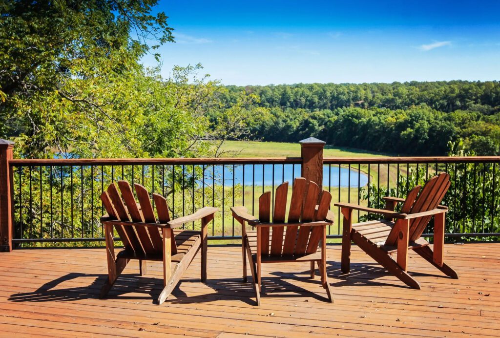 Corner deck with black railing surrounded by dense trees in shaded backyard.