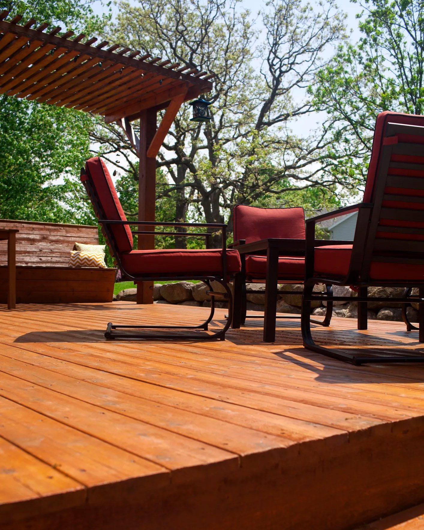 Wood deck with partial pergola cover and built-in bench seating featuring throw pillows.