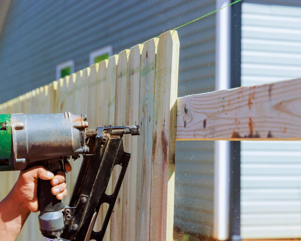 Trinity Fence & Deck crew member securing new fence panel during repair job Fence repair in progress using nail gun on wood panel by Trinity Fence & Deck in Austin, TX