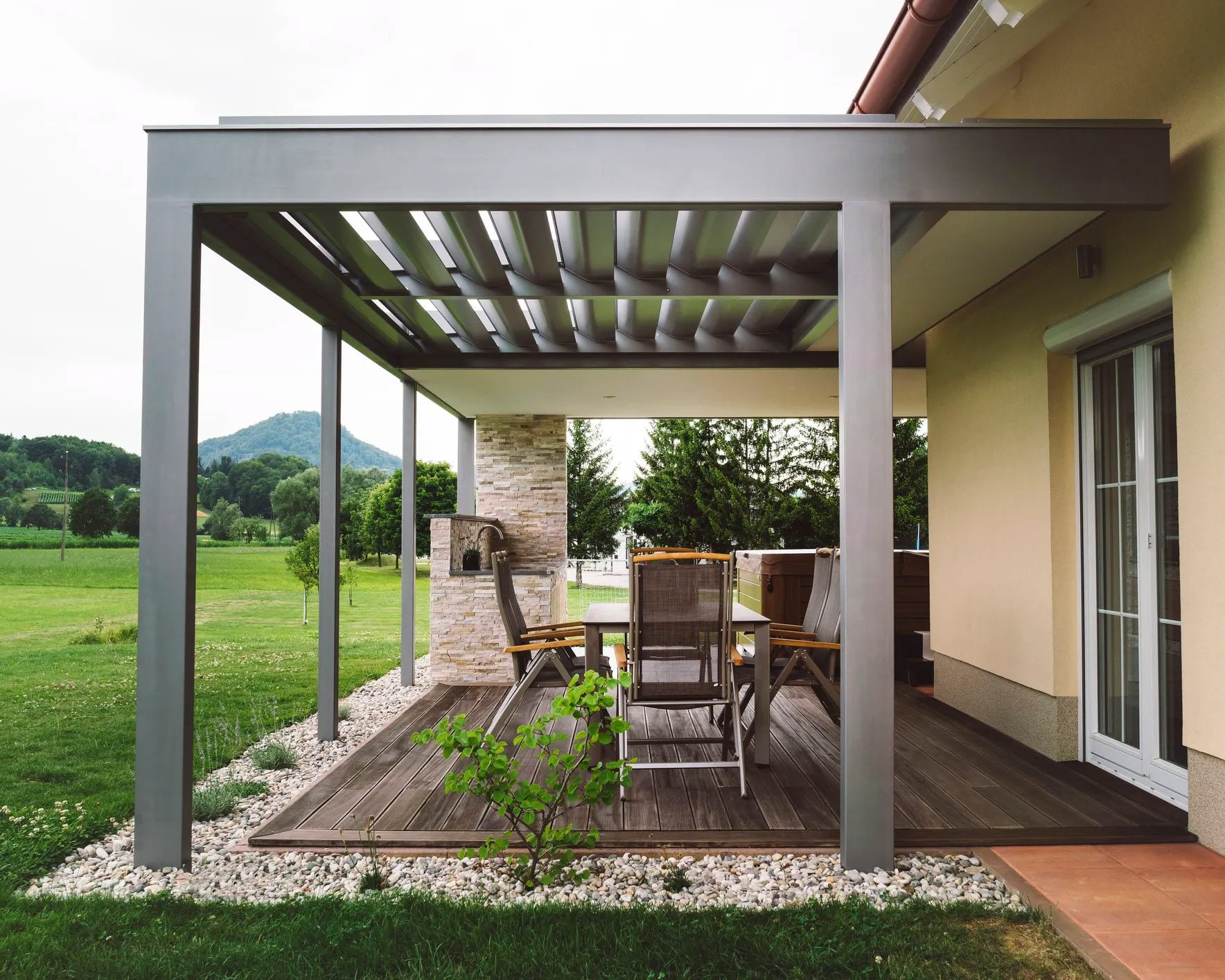Louvered roof over backyard patio table and green lawn