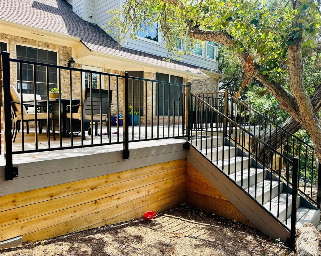 Wide elevated composite deck with black iron railing perimeter and wood skirting.