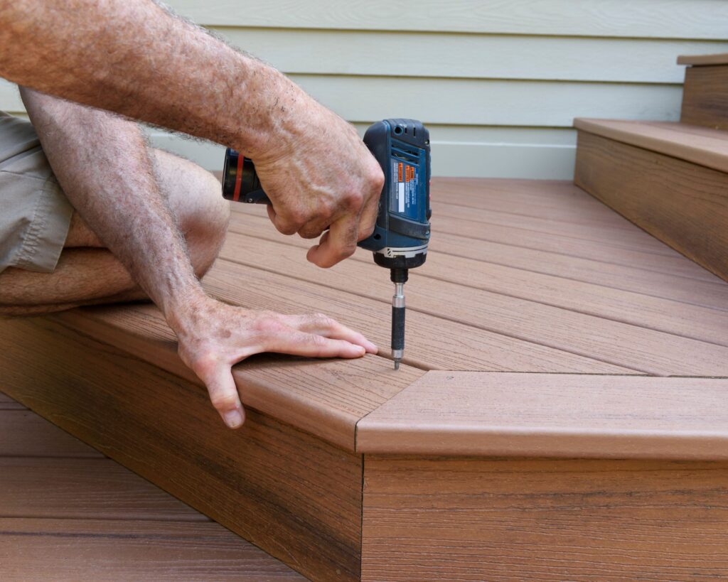 Deck repair in Austin progress – secure composite stair tread Close-up of deck repair with drill securing composite plank on stair tread