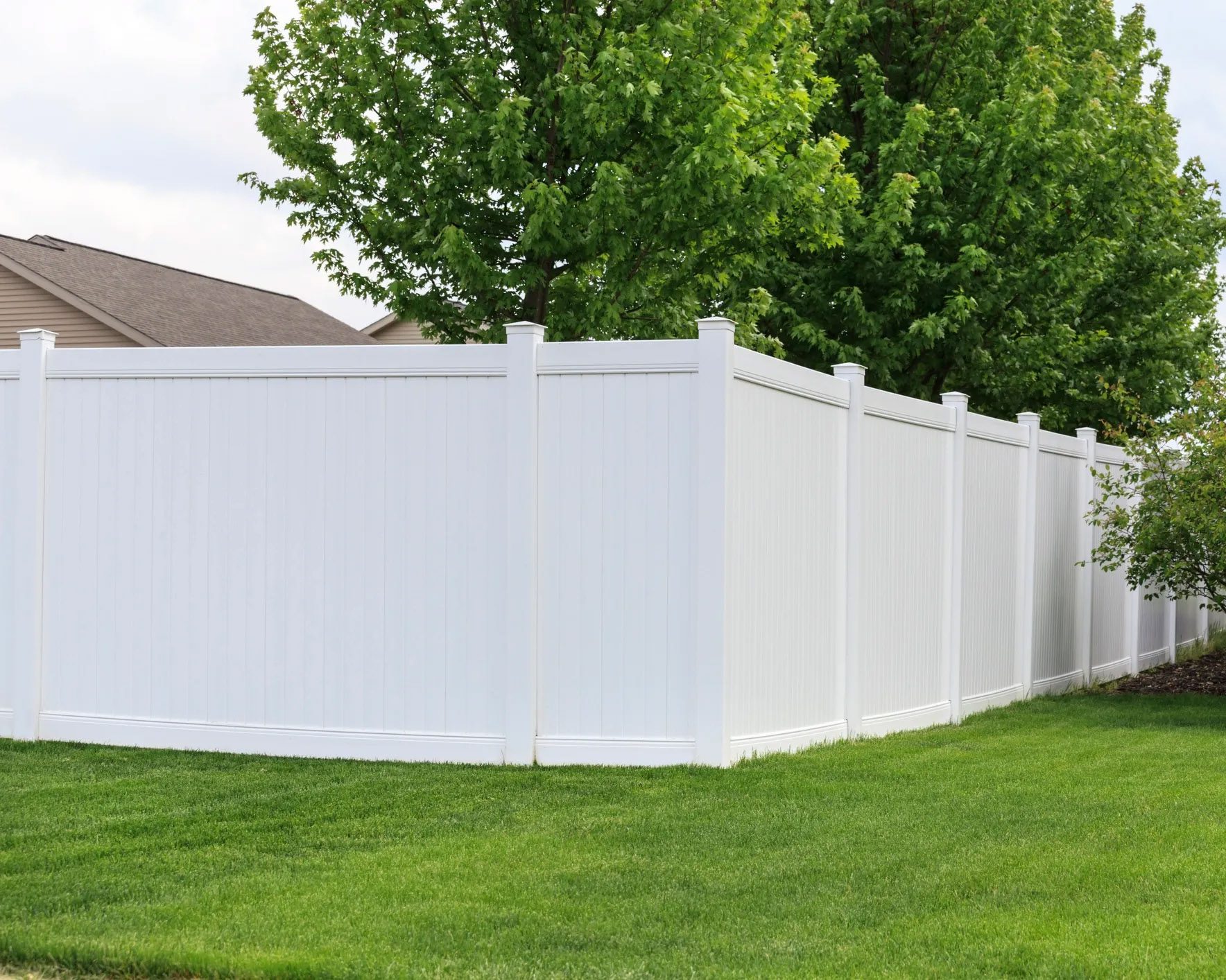 Solid white vinyl fence with green trees in background