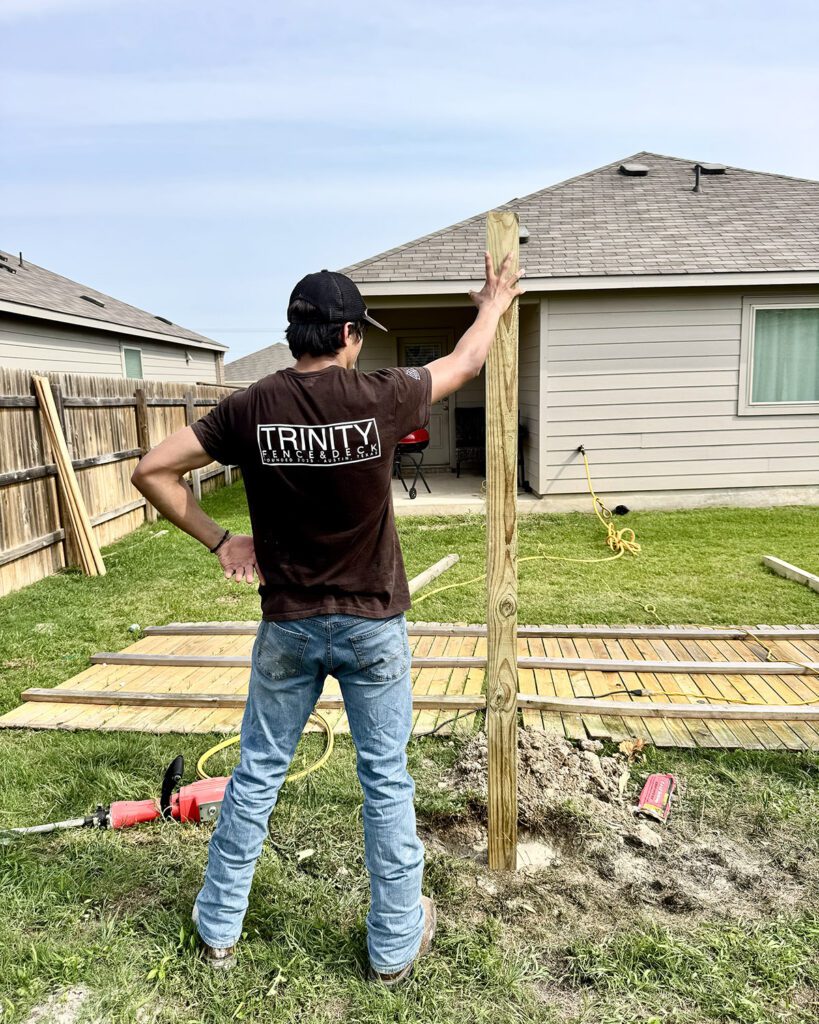 Trinity Fence & Deck crew member setting a new cedar fence post during a backyard repair project in Central Texas.