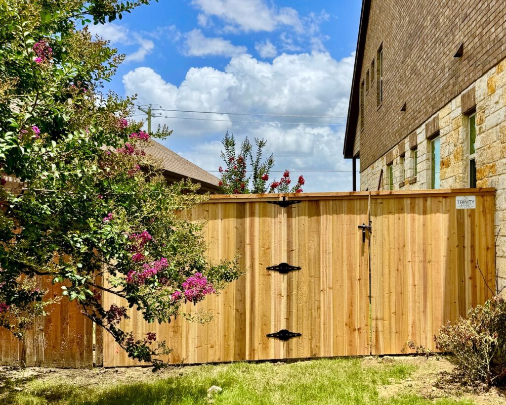 Custom backyard deck with iron railing | Trinity Fence & Deck Gallery Austin Cedar gate framed by blooming crepe myrtles and a stone façade