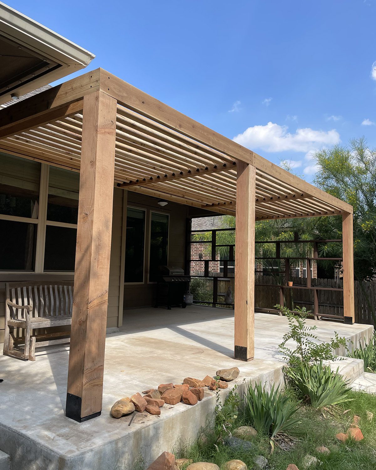 Side view of a cedar pergola installed on a concrete slab with garden landscaping in the foreground.