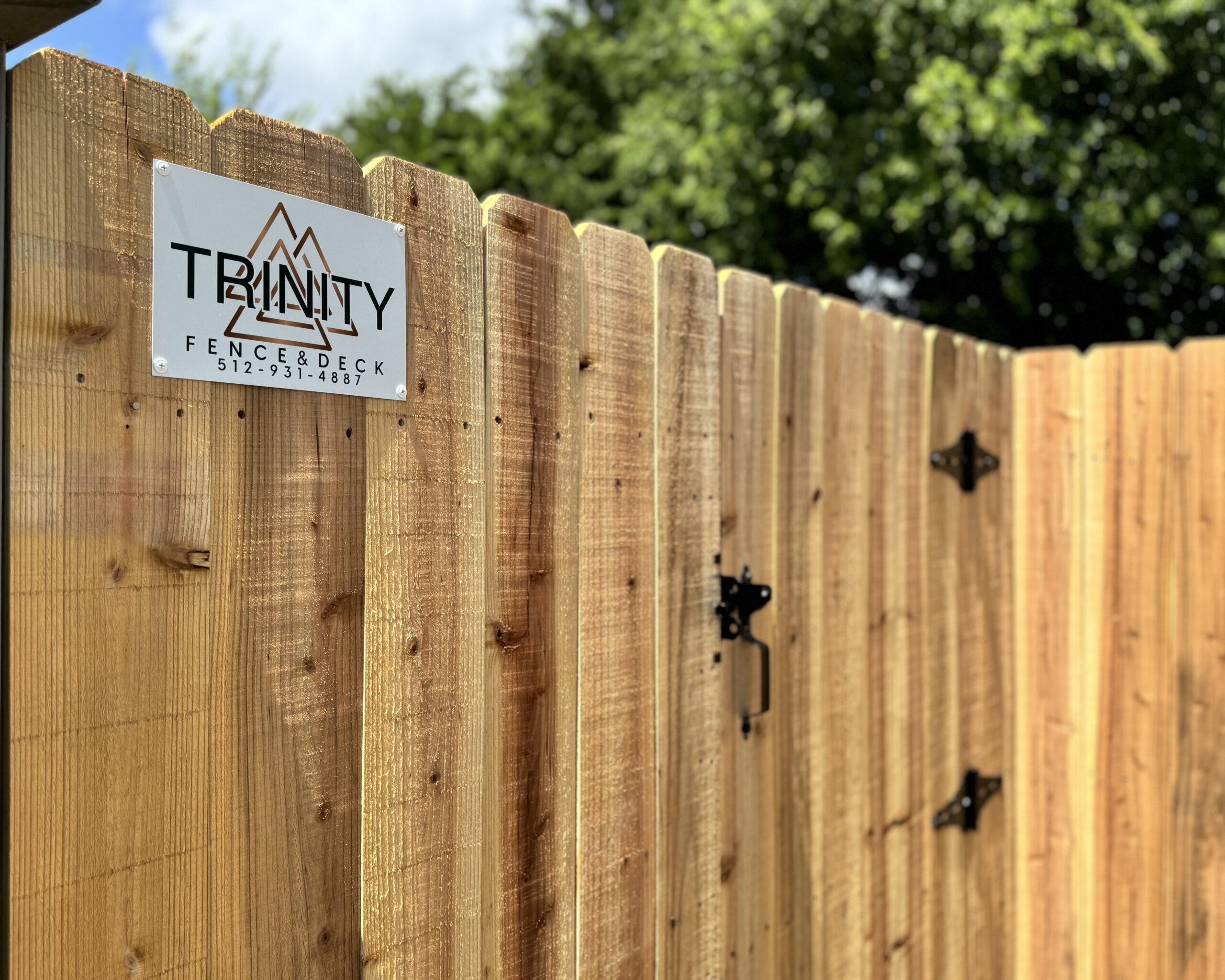 Trinity Fence & Deck logo sign mounted on a cedar privacy fence