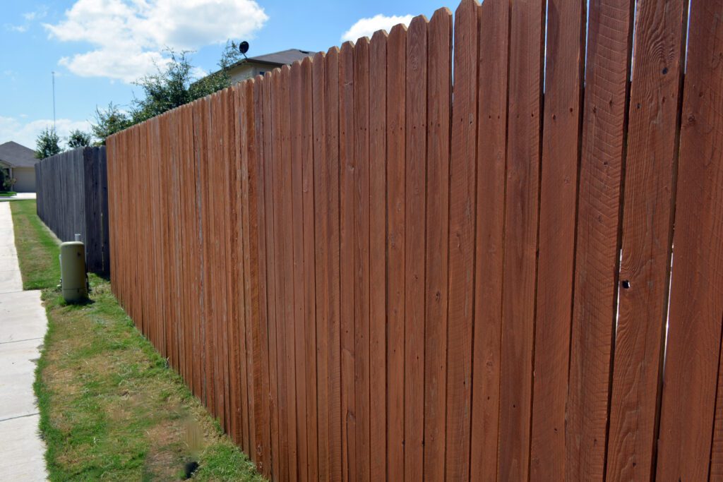 Cedar fence with warm-toned stain bordering flower beds and iron gate