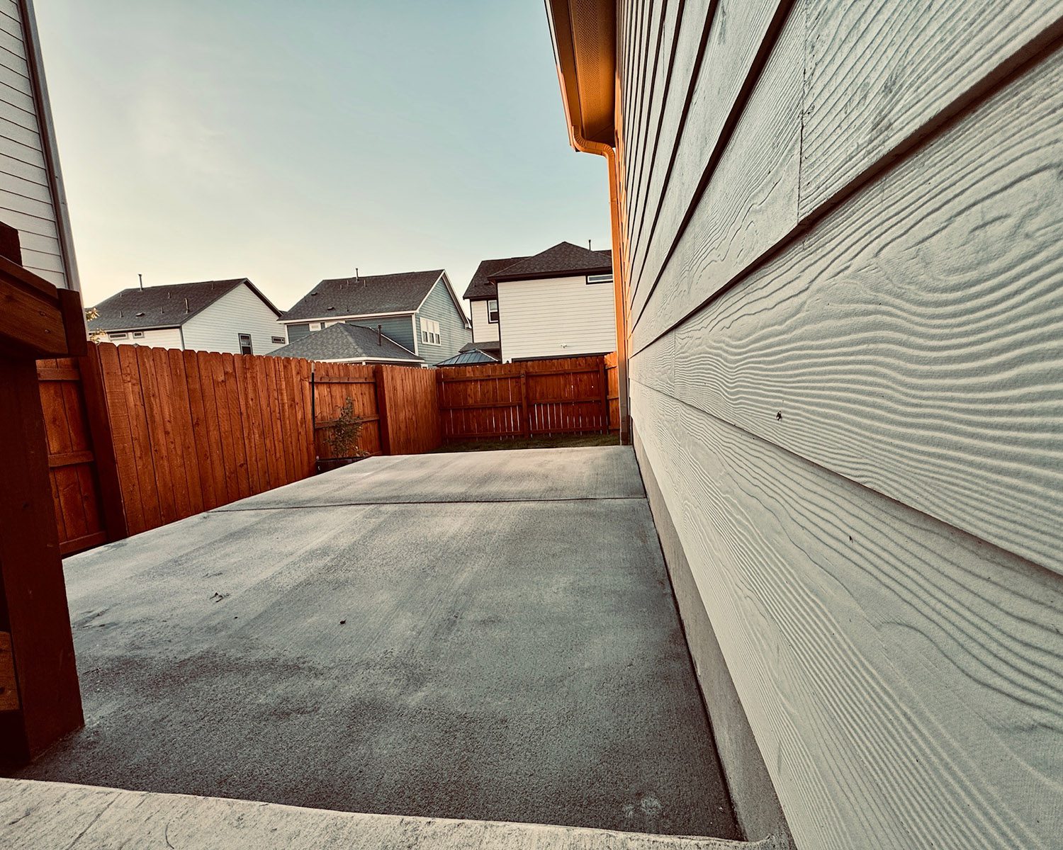 Side perspective of concrete patio running along home with wood fencing in background.