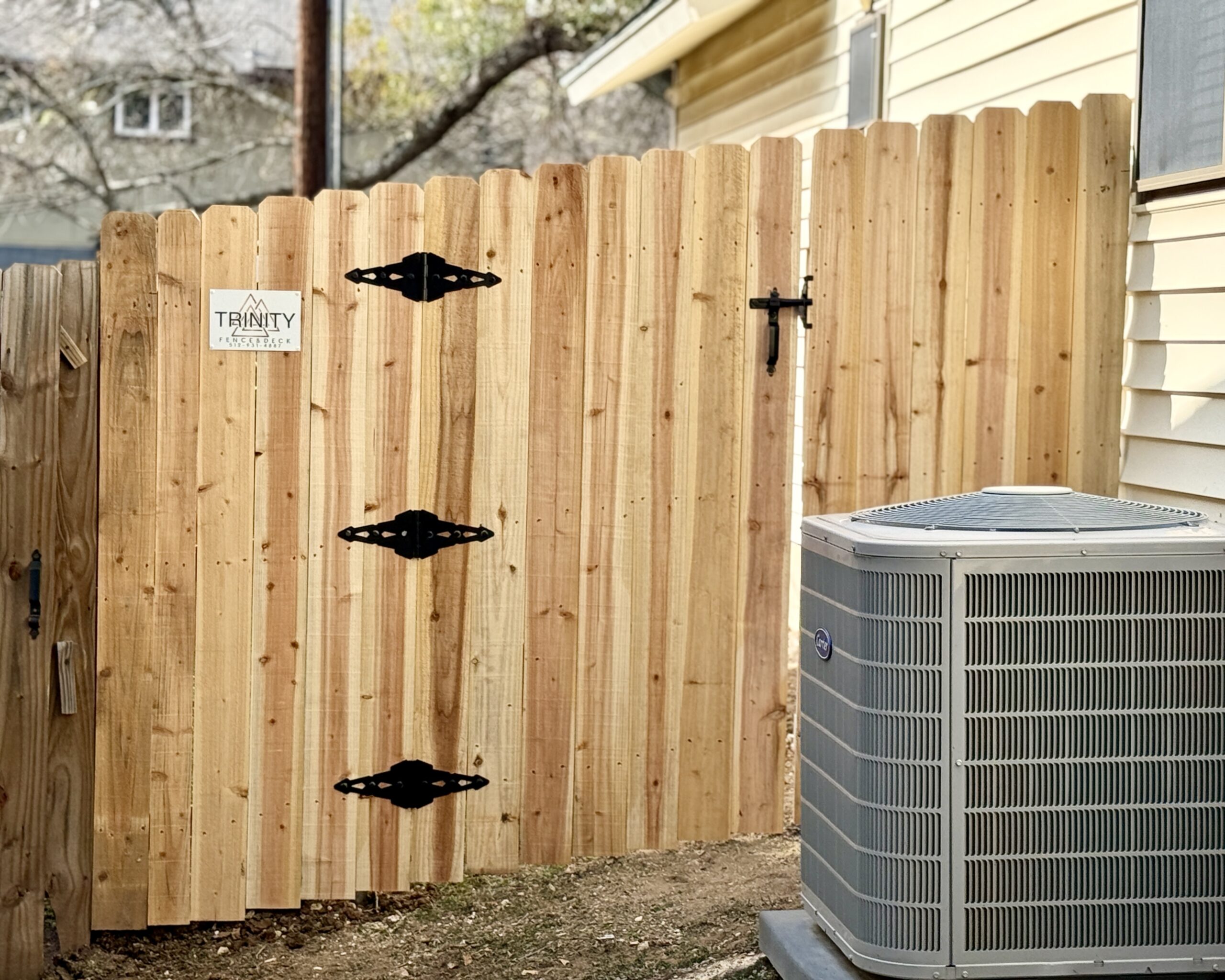 Completed cedar privacy fence gate with steel hardware and Trinity Fence & Deck signage